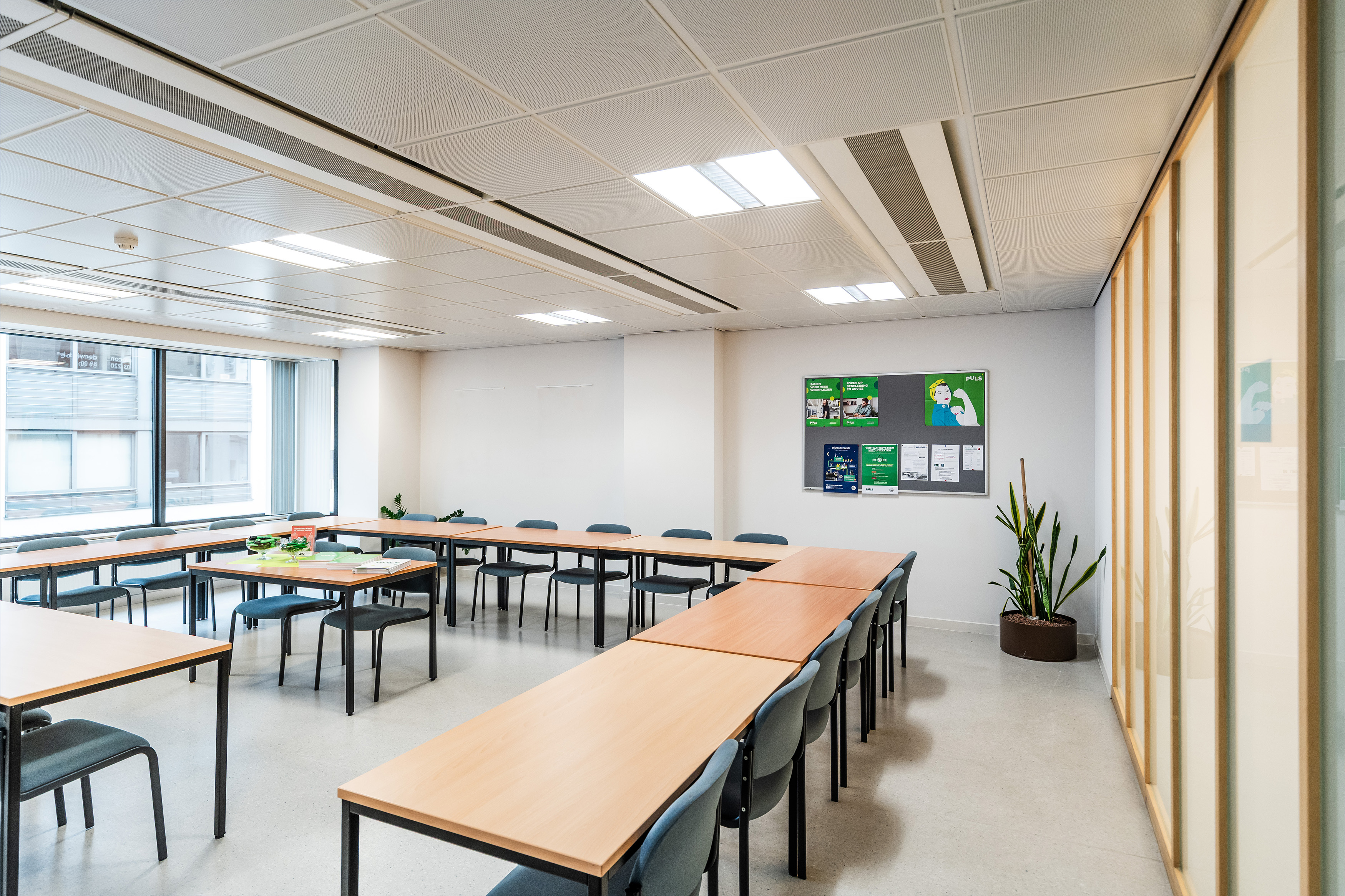 Zicht in een lokaal waar tafels in een u-vorm opgesteld staan met stoelen rondom. Bedoeld als studeerplekken