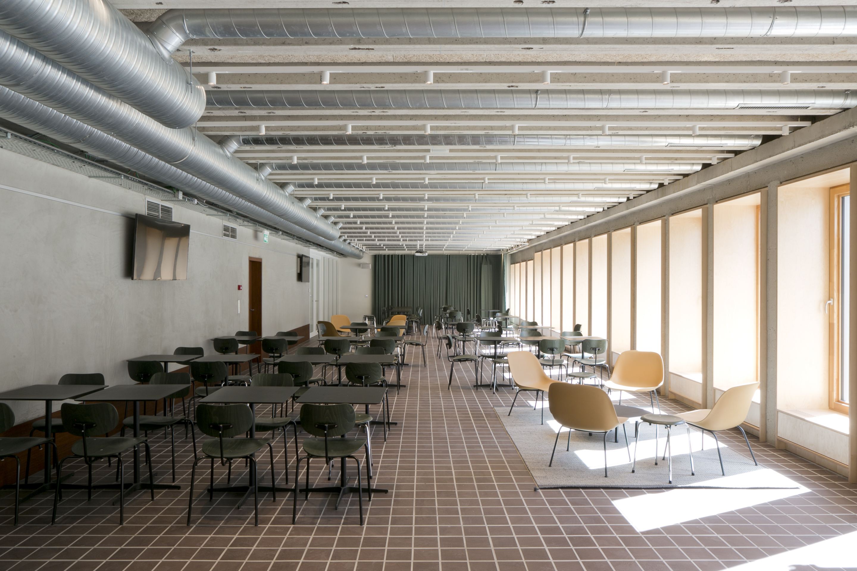 Binnenzicht op een studeerruimte bij De Pit waar stoelen en salonnetjes staan opgesteld. Rechts de hoge ramen met veel lichtinval