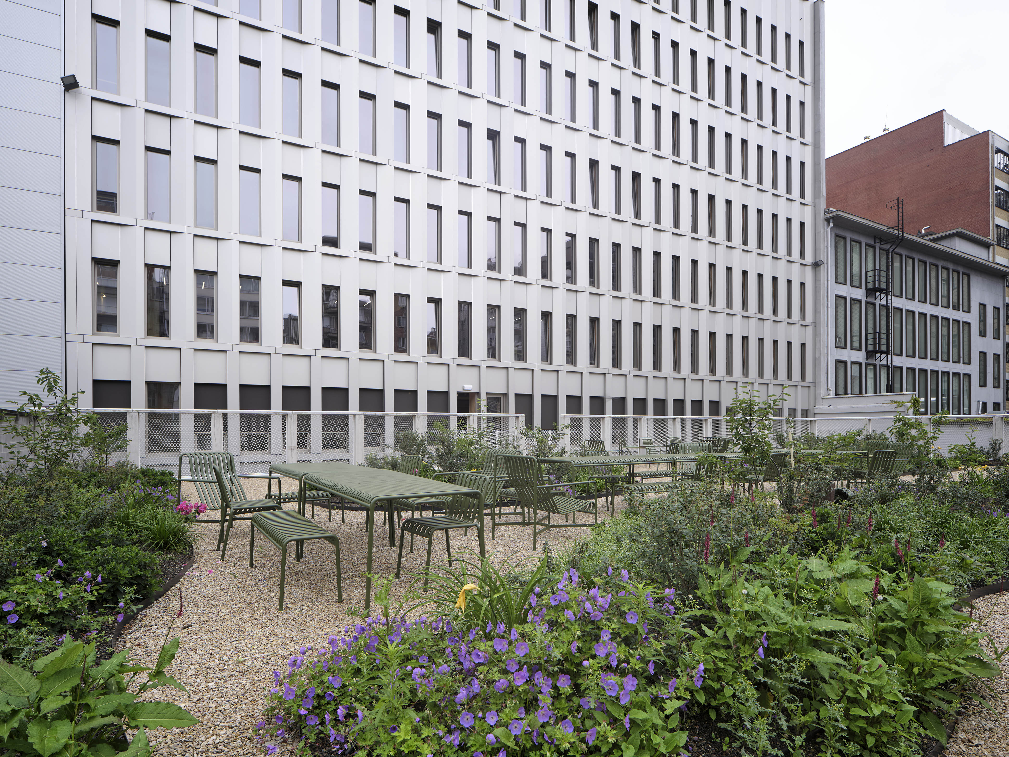 Zicht vanop het terras van kantoorgebouw De Pit richting het gebouw. Op de voorgrond beplanting en bankjes.