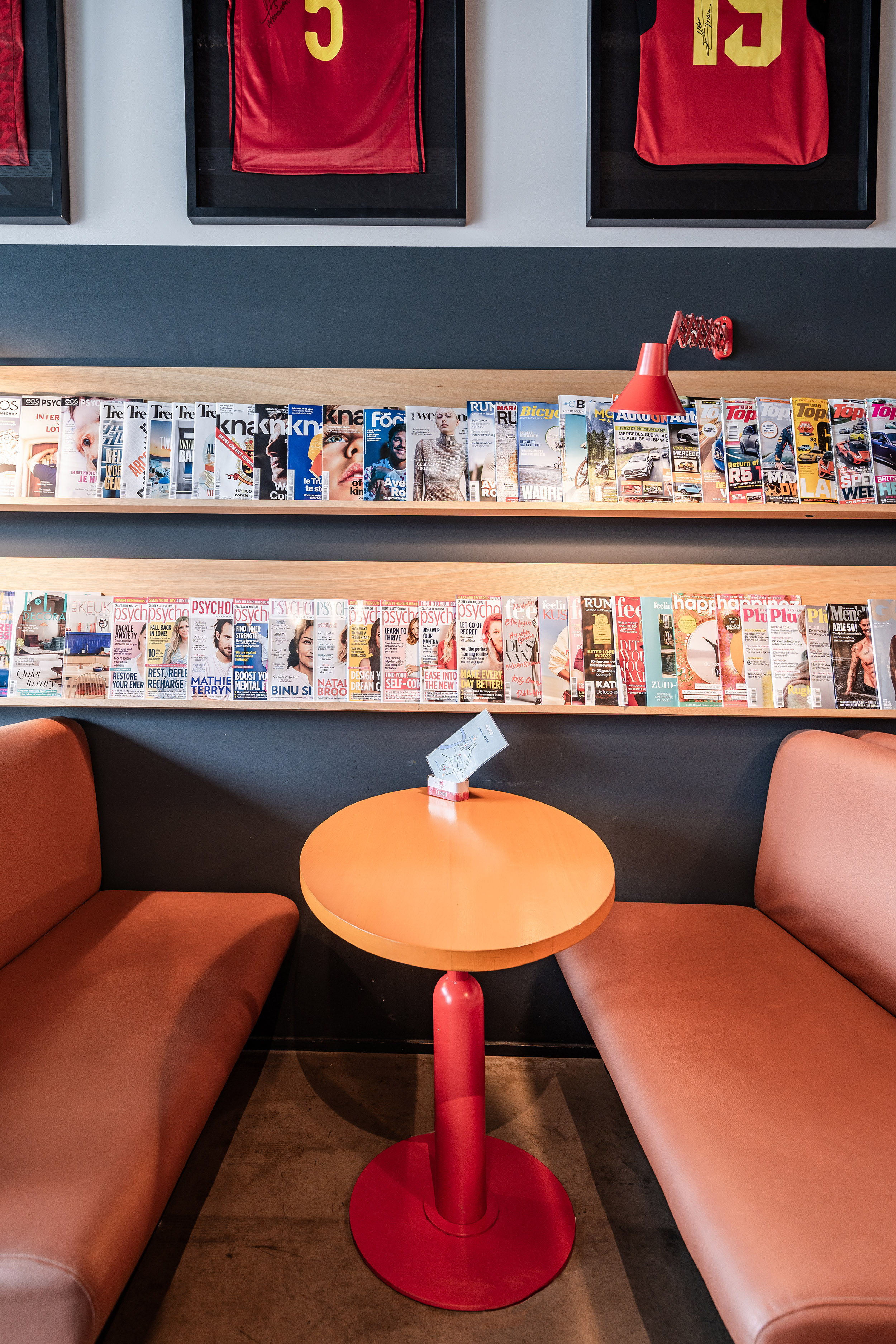 Zicht op twee zitbanken opgestond rond een rond tafeltje met op de achtergrond magazines opgesteld in een schap