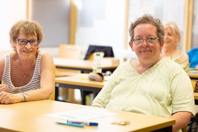 twee volwassen vrouwen in een klaslokaal kijken glimlachend in de lens