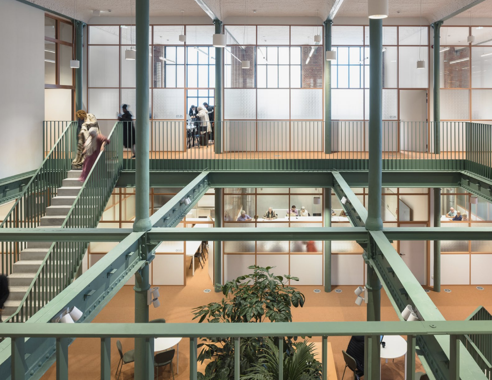 Open ruimte met veel glas, groene planten en een stalen trap