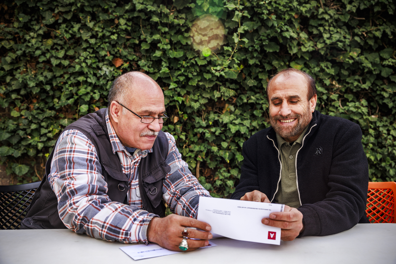 Twee mannen zitten neer. De ene heeft een brief in zijn handen.