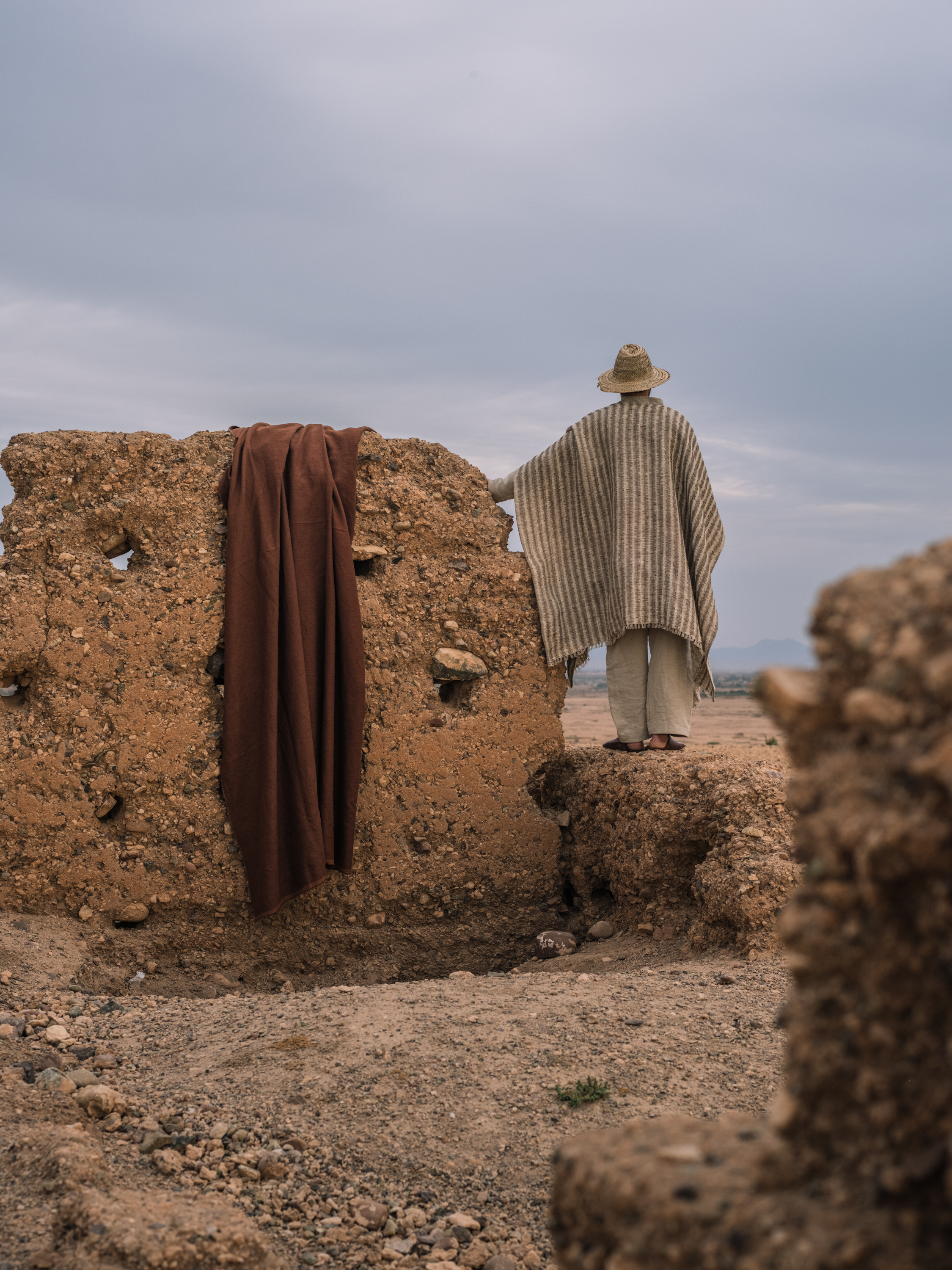 Man wearing a cape made of TARANGA YP26001 fabric, drape GRAVITAS YP26010 photographed in the Moroccan desert for the Azimuth 2026 fabric collection by Designs of the Time