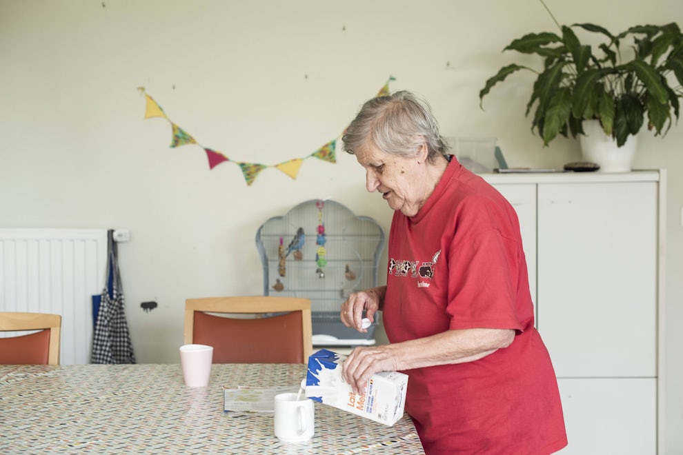 Bewoner woondienst senioren giet melk in een tas.