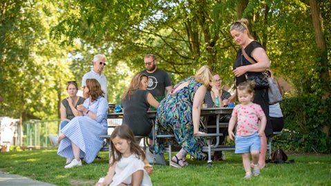 Een groep ouders babbelen aan een picknicktafel terwijl kinderen spelen