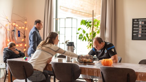 Medewerker en drie bewoners zitten samen aan de eettafel voor een koffiemoment