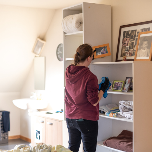 Vrouw staat met de rug naar de camera en stoft fotokaders af in een studio.