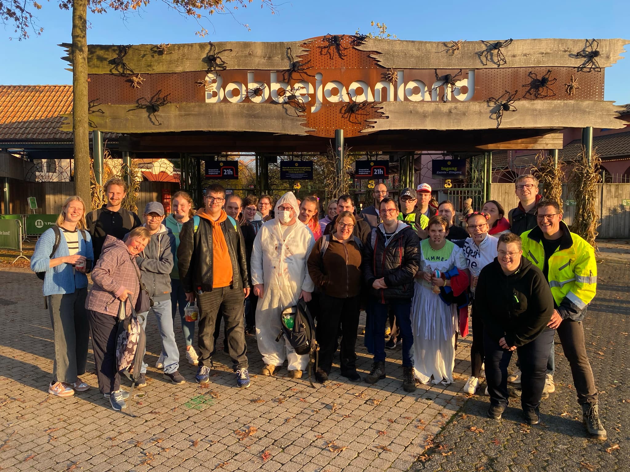 Een vrolijke groep volwassenen poseert voor de ingang van Bobbejaanland tijdens een zonnige uitstap.