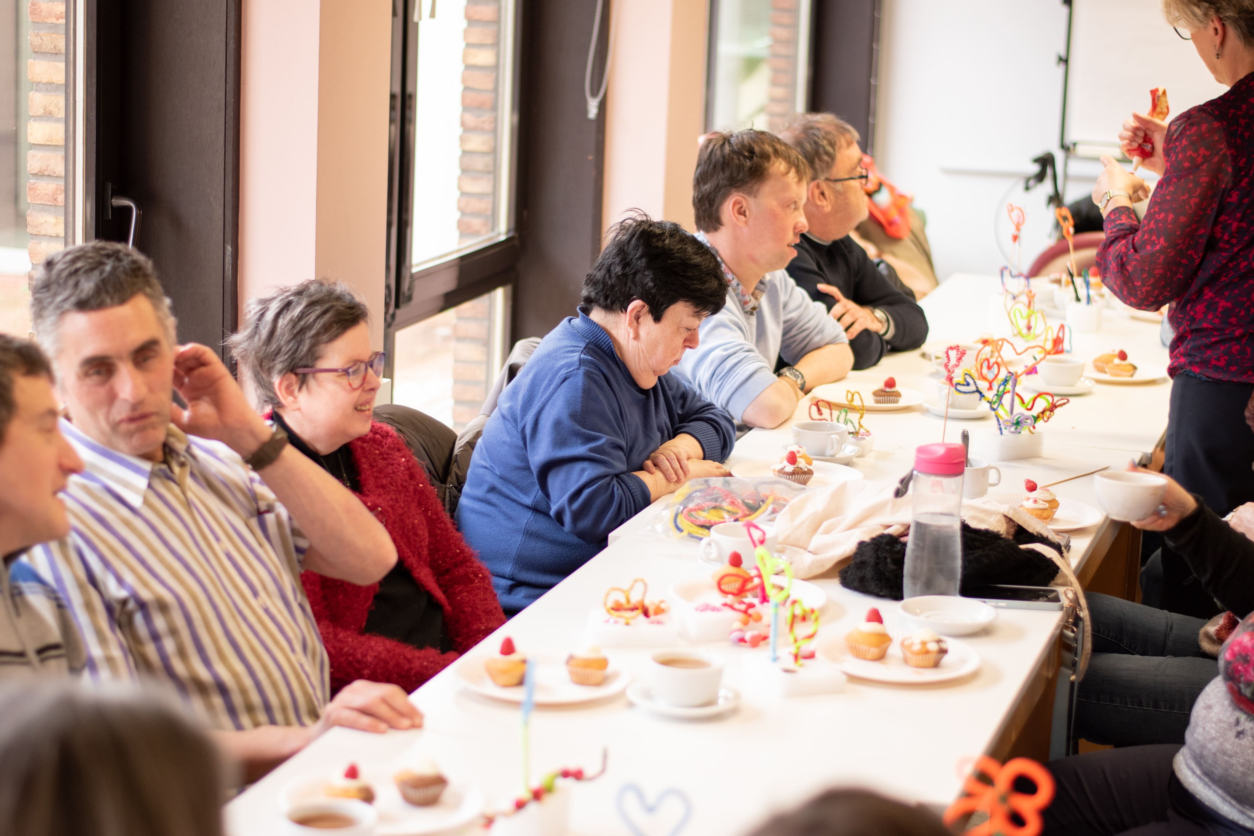 Volwassenen zitten aan een lange tafel plezier te maken en cupcakes te eten.