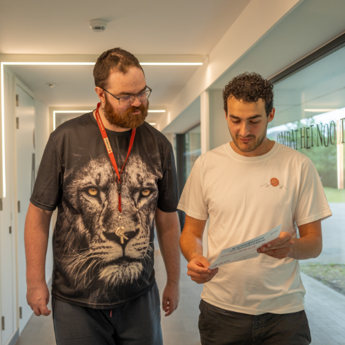 Mobiel ambulant begeleider loopt in de gang met een cliënt en ze nemen samen papieren door.