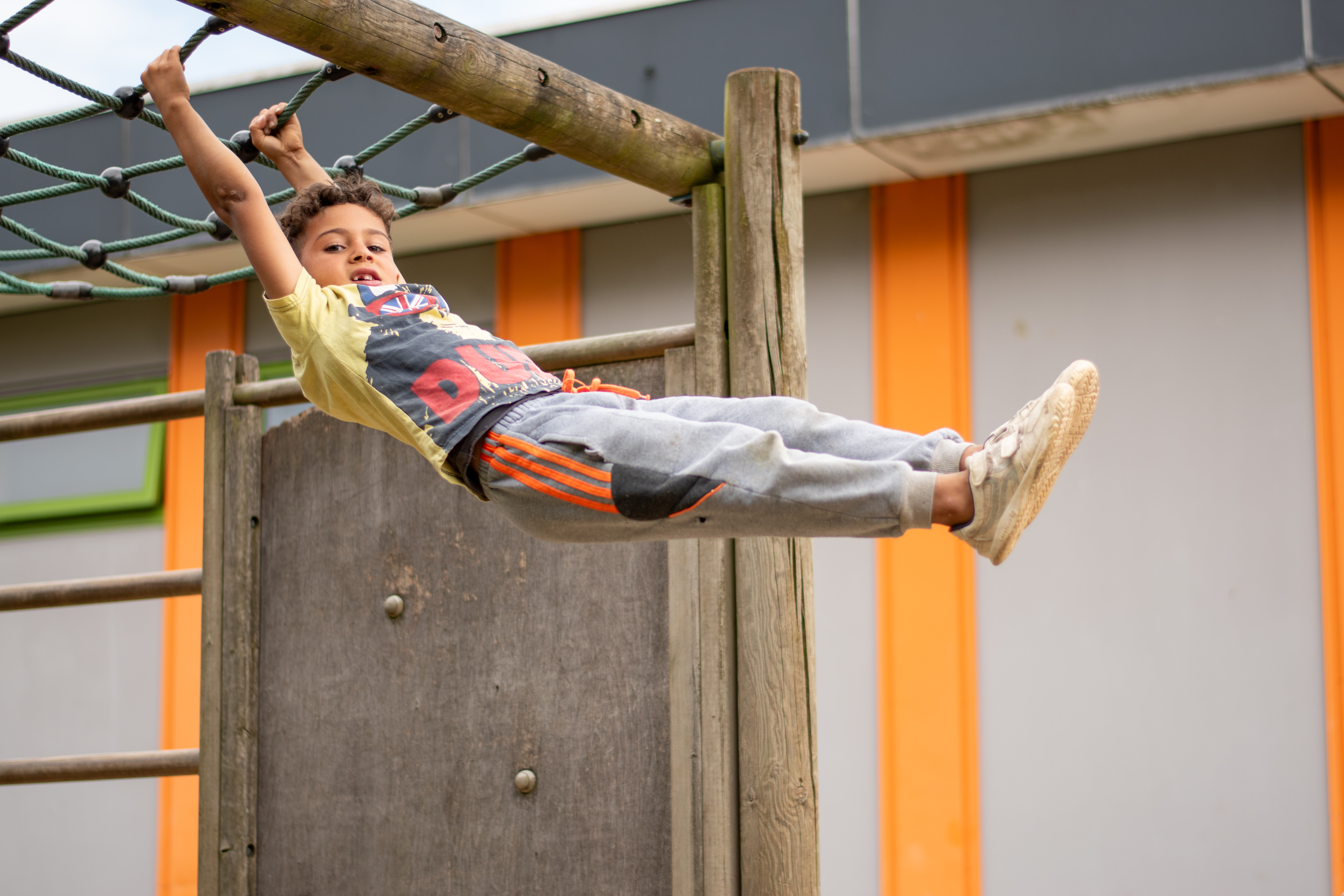 Een jonge jongen hangt met beide handen aan een klimnet op een speeltoestel.