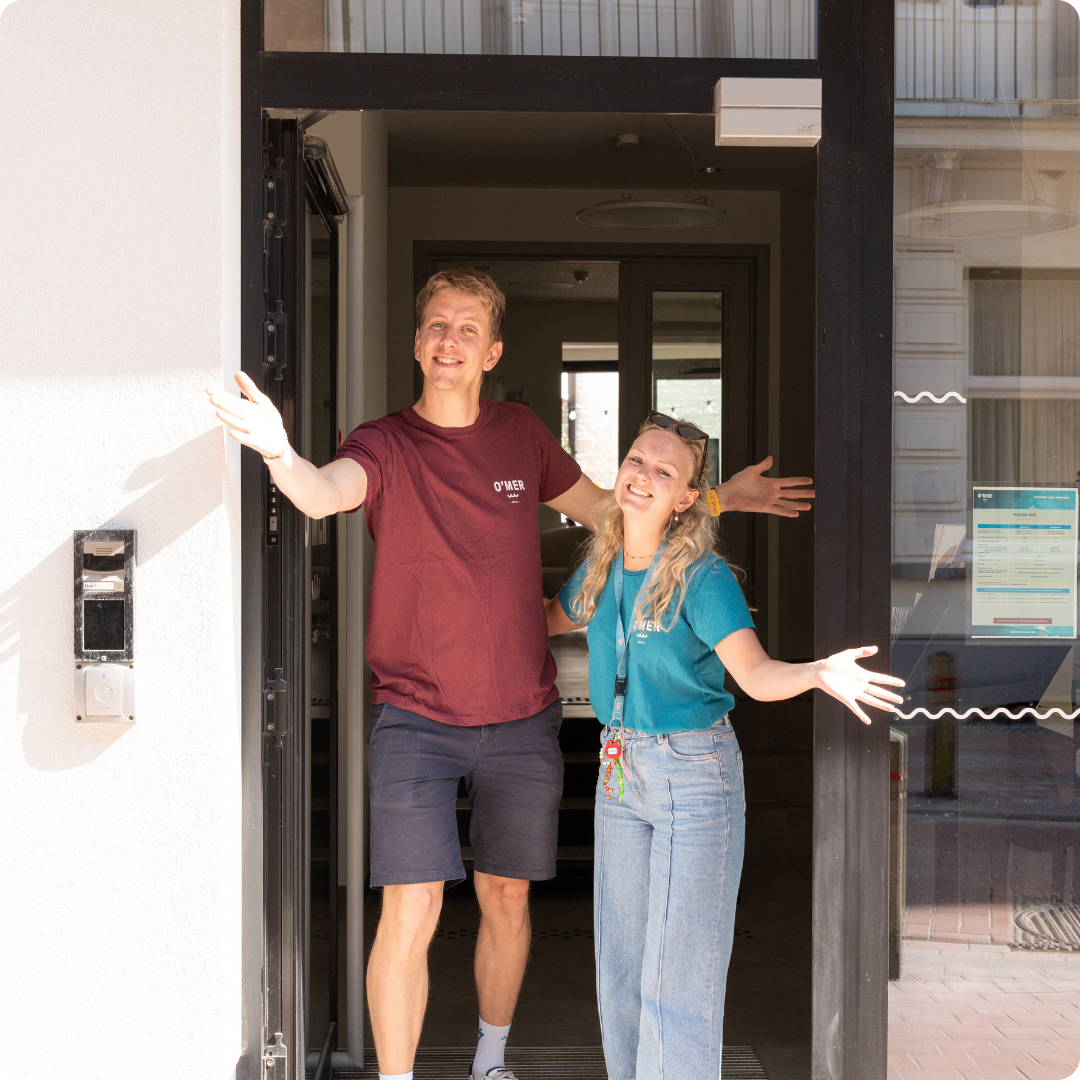 Jonge mannelijke en vrouwelijke begeleidster van Hotel O'mer staan verwelkomend in het deurgat