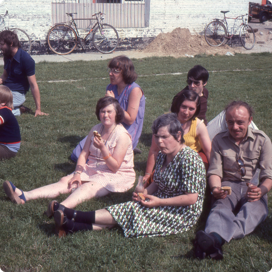 Groep mannen en vrouwen die een wafeltje eten in een grasveld