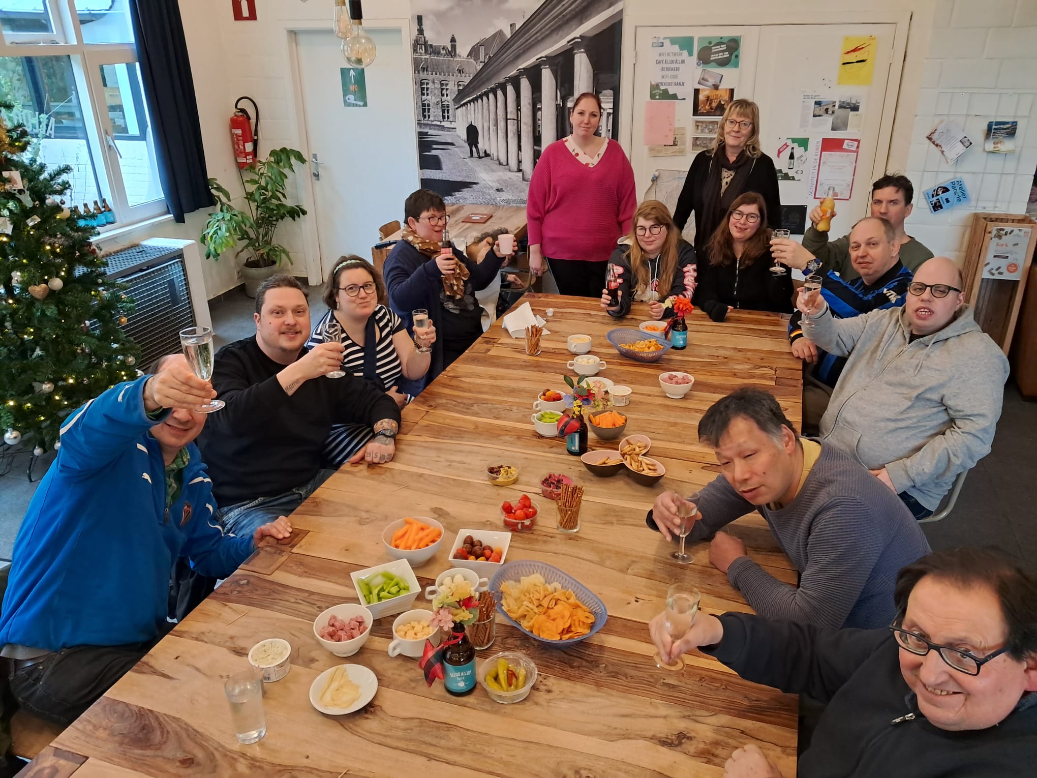 Gezellige groep mensen rond een lange tafel met eten, lachend naar de camera.