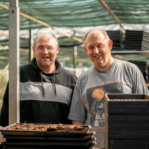 Twee mannelijke cliënten werken in een serre en kijken lachend.