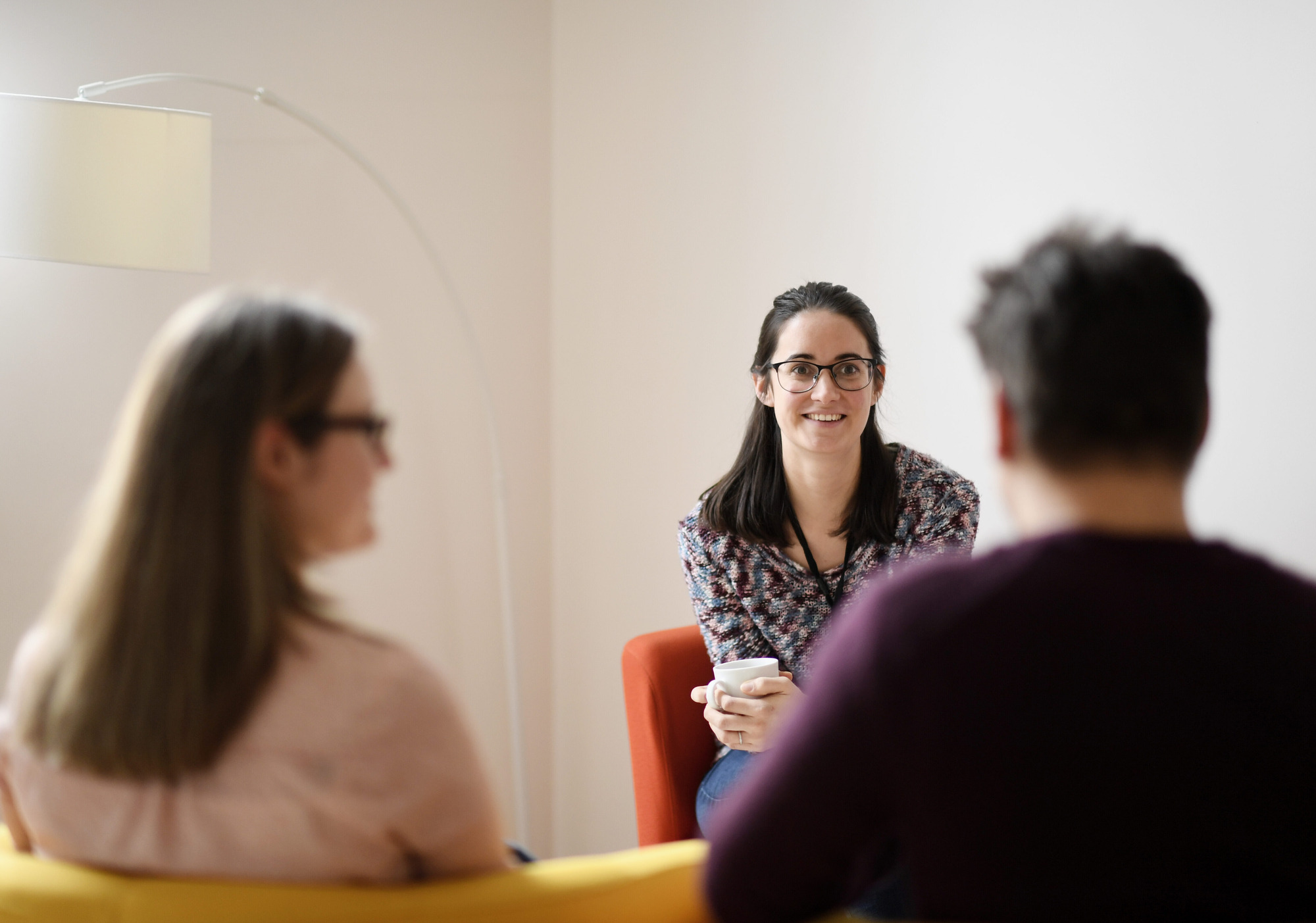 Vrouwelijke hulpverlener met bril in gesprek met 2 ouders.