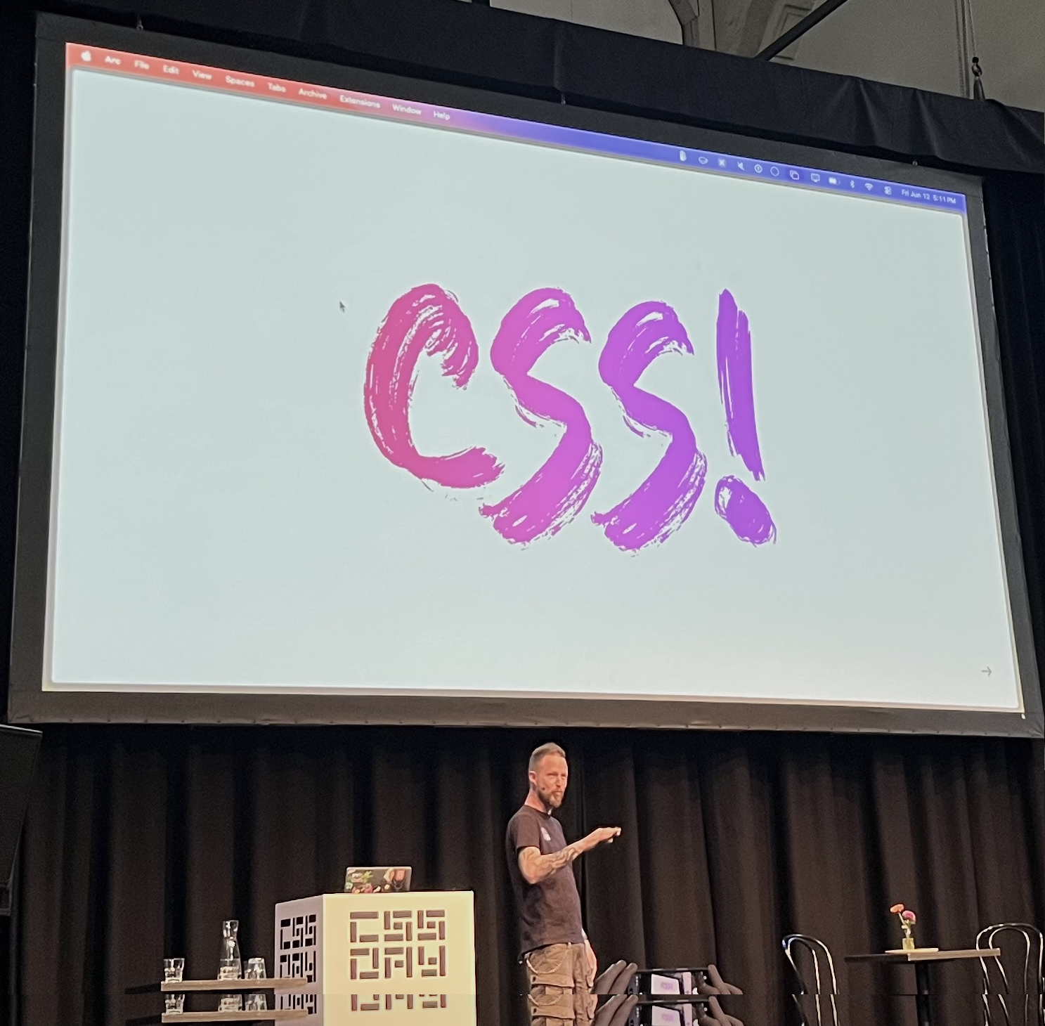 Adam Argyle very excitedly talking about CSS with a very bright prink to purple CSS logo in the background