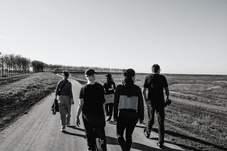 5 collega's van EHBJ op wandel, zwart wit foto, langs achteren genomen. Ze kijken allen in de verte.